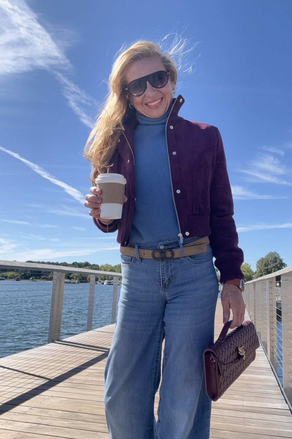A wine faux suede bomber worn open over a blue knit with jeans
